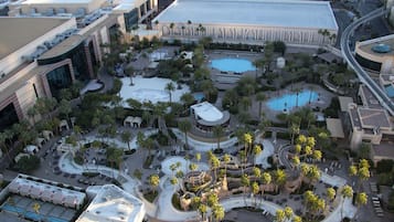 An aerial view of a hotel complex with multiple buildings, a central courtyard with palm trees, and a large swimming pool.
