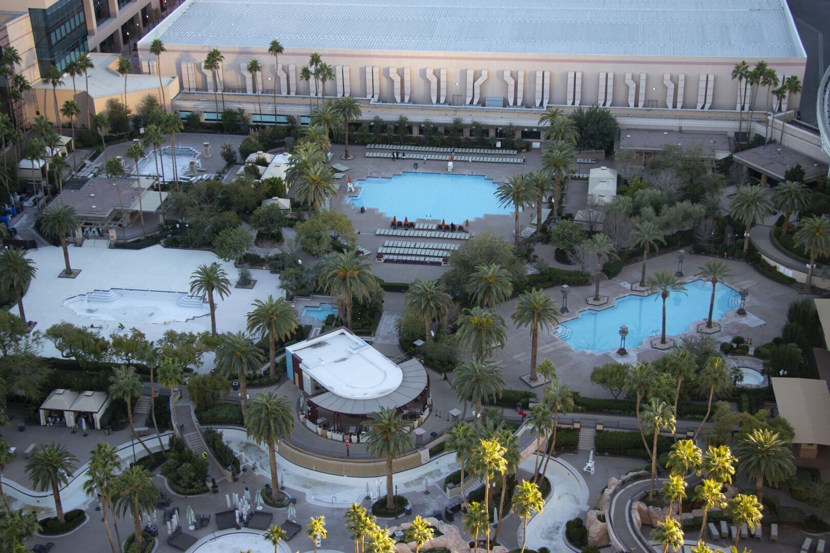 A hotel with multiple swimming pools, palm trees, and a large building in the background.