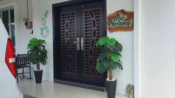 A hotel entrance with a dark wooden door, potted plants, a bench, and a sign that reads "Nur Hartamas". - Nur Hartamas Homestayportdickson (Port Dickson)