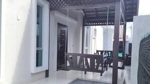 A covered patio area with a swing set, a small lawn, and a building with a tiled roof. - Nur Hartamas Homestayportdickson (Port Dickson)