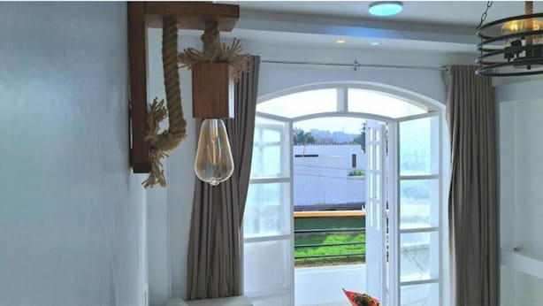 Ein Zimmer mit großem Fenster, einer Pendelleuchte und Vorhängen.