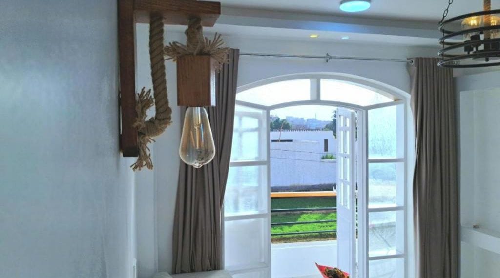 Une pièce dotée d’une grande fenêtre, d’un luminaire suspendu et de rideaux.