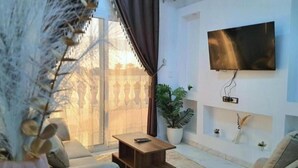 Un salon avec un canapé, une table basse, un téléviseur fixé au mur et une plante en pot.