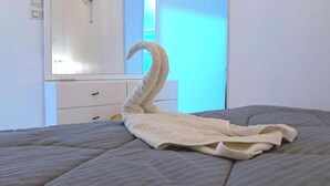 Ein Bett mit einer zu einem Schwan gefalteten Decke, eine weiße Kommode und ein Fenster mit blauer Tönung.