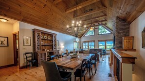 A spacious dining area with a wooden table and chairs, a chandelier, and a stone fireplace. - Mountain Views, Hot Tub & Resort Amenities in Sapphire, NC (Sapphire)