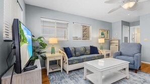 A living room with a sofa, a coffee table, a TV, and a ceiling fan. - 50 Seahorse Beach House #4: Pool & Walk to Beach! (Fort Myers Beach)