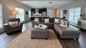A spacious living room with a large sectional sofa, a coffee table, and a modern ceiling fan. - Chicopee House ~ Your 4 bd, 3 bath, Athens Getaway 1-mile to Sanford Stadium! (Athens)