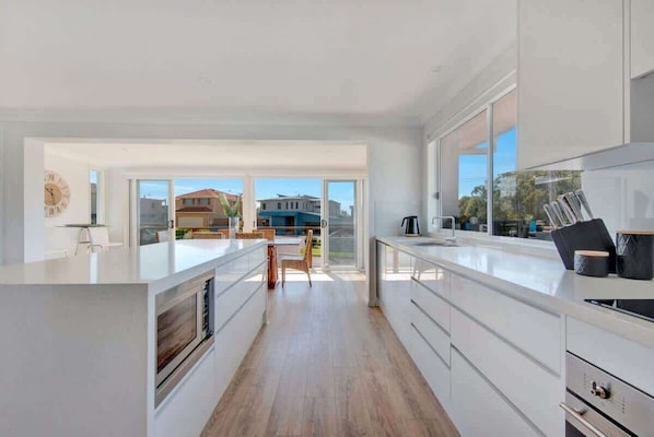 A modern kitchen with a large island, white cabinetry, and a view to the outside.