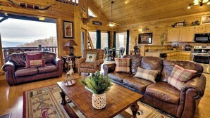 A cozy cabin interior with a large wooden dining table, leather sofas, and a kitchen area.
