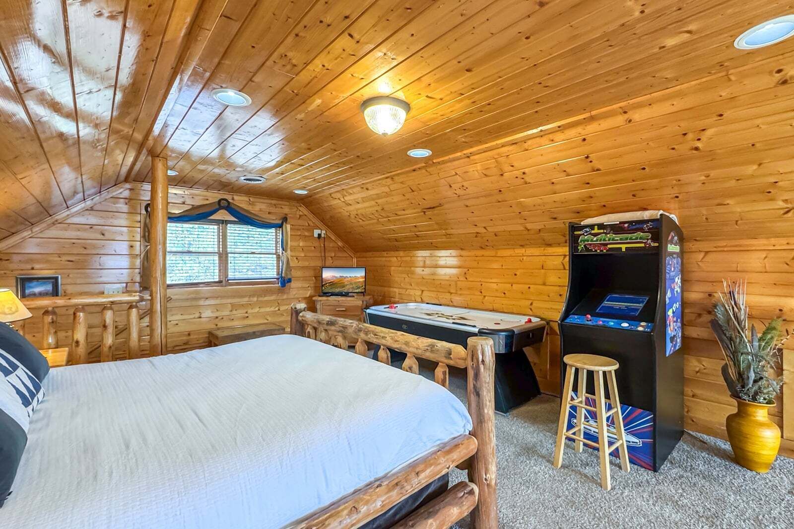 A cozy cabin room with a bed, a pool table, a dartboard, and a video game machine.