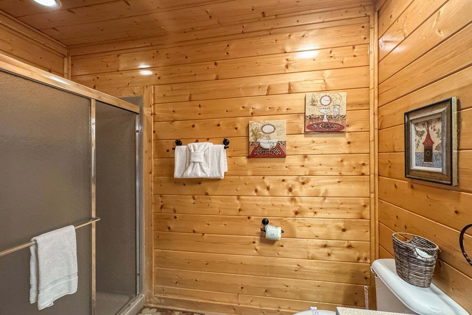 Puupaneelilla verhoiltu kylpyhuone, jossa on suihku, pyyhkeet ja seinillä tauluja.