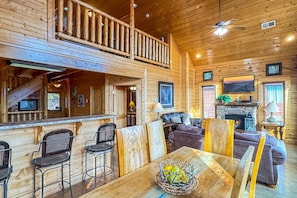 A wooden cabin interior with a dining area, bar, seating, and a fireplace. - On Eagles Wings・Panoramic Views・Hot Tub・Game Room・Resort Access (Sevierville)