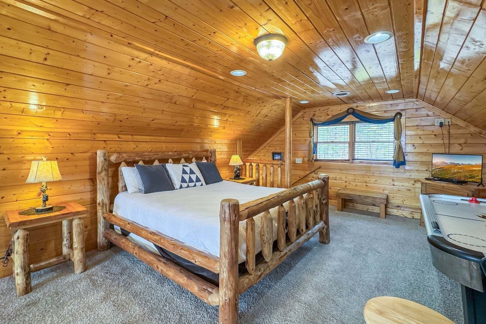 A wooden cabin bedroom with a bed, bedside tables, a desk, and a window.