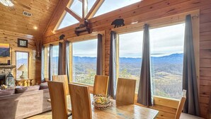 A log cabin interior with a dining area, wooden furniture, large windows, and a fireplace. - On Eagles Wings・Panoramic Views・Hot Tub・Game Room・Resort Access (Sevierville)