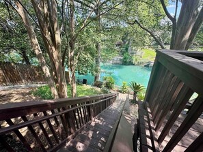 A wooden deck overlooking a turquoise body of water, surrounded by trees. - Wasser Lodge #201 | Sleeps 4 | WIFI (New Braunfels)