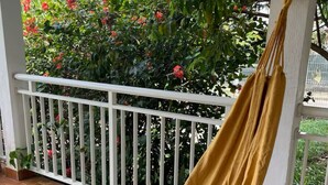 A hammock on a balcony with a white railing, surrounded by lush green foliage and red flowers. - 3-bedroom villa - island center (Fort-de-France)
