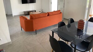 A modern living room with a sofa, a glass dining table, and a flat-screen TV mounted on the wall. - 3-bedroom villa - island center (Fort-de-France)