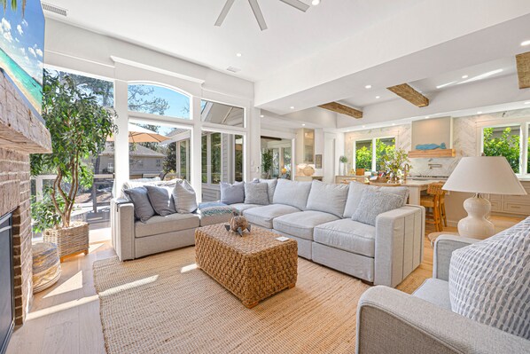 A spacious living area with a large sectional sofa, a woven coffee table, and a kitchen in the background.