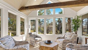 Une véranda avec de grandes fenêtres, des poutres en bois au plafond et des meubles aux motifs décoratifs.