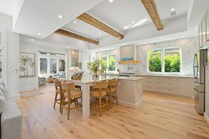 A spacious kitchen with wooden beams, a large island with bar stools, and a view of greenery outside.