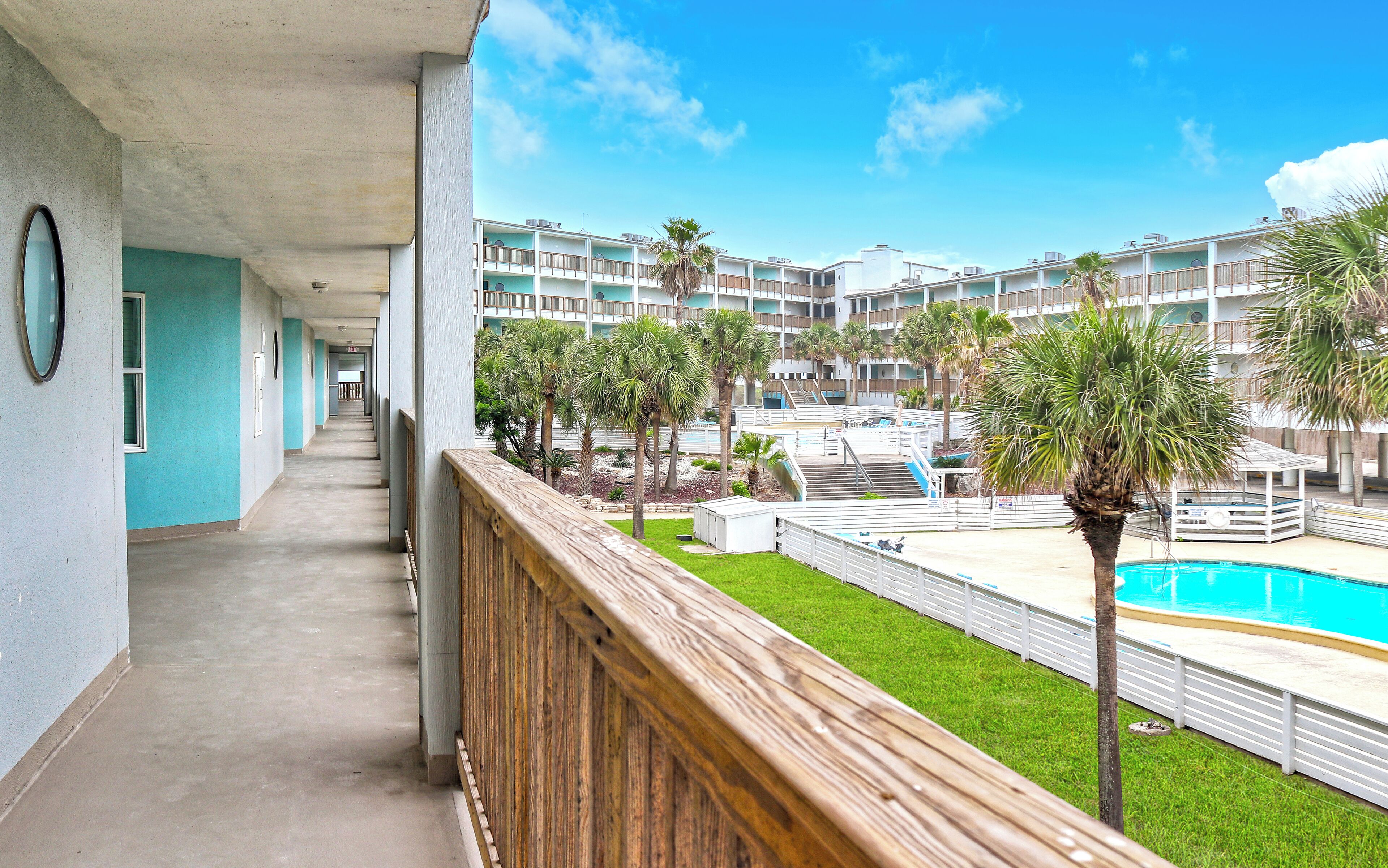 A hotel corridor with a pool area, including a pool, palm trees, and a view of the building's exterior.