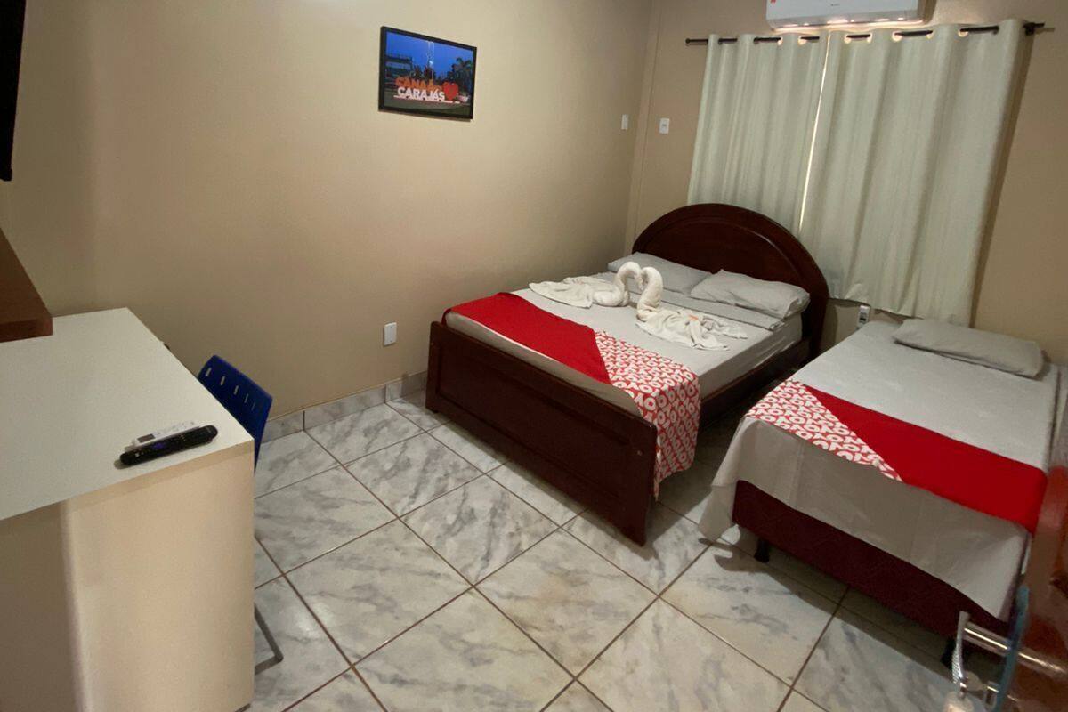 Ein Hotelzimmer mit zwei Betten, einem Schreibtisch, einem Stuhl, einem Bild an der Wand und einer Klimaanlage.