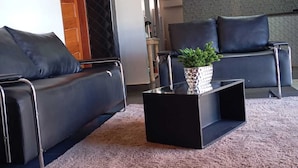 Ein modernes Wohnzimmer mit zwei schwarzen Ledersofas, einem Glastisch mit Pflanze und einem strukturierten Teppich.