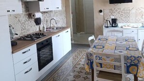 A compact kitchen with white cabinets, a gas stove, and a patterned rug. - Anninedda rooms (Palermo)