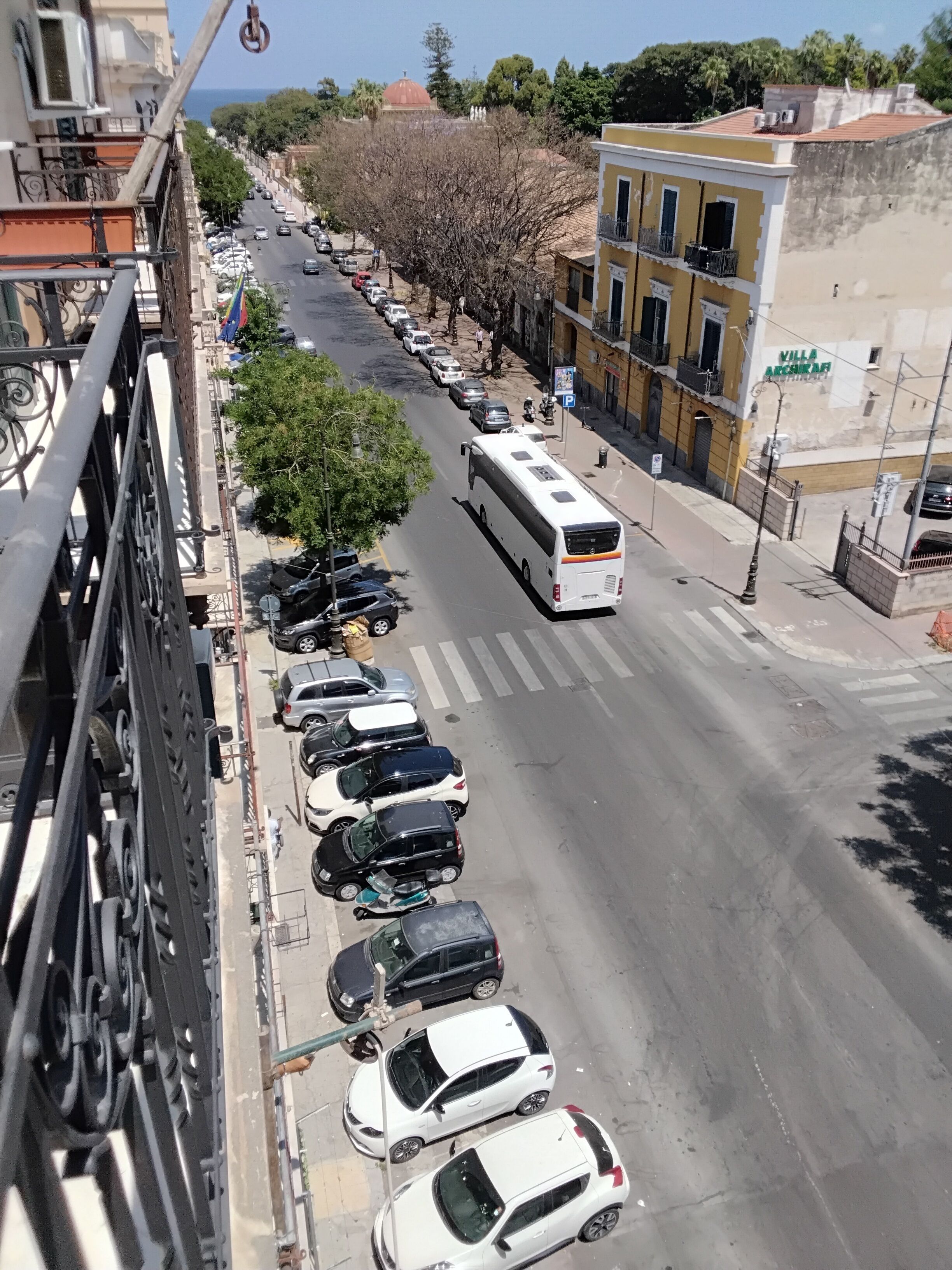 Vista de la calle con fila de autos estacionados, un autobús y edificios.