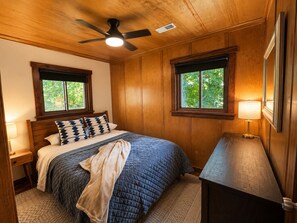 A bedroom with a bed, a nightstand, a lamp, a ceiling fan, and two windows. - Lakefront Mid-Century Cabin • Private Dock Hot Tub • Fire Pit • Modern Retreated (Dry Ridge)