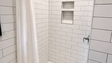 Une douche avec des murs recouverts de carreaux blancs, un sol à motifs en chevrons et un pommeau de douche.