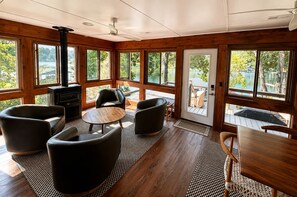 A cabin interior with a fireplace, seating area, and large windows offering views of a lake.