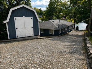 A gravel driveway leading to a blue building with a white garage door and a small shed. - Lakefront Mid-Century Cabin • Private Dock Hot Tub • Fire Pit • Modern Retreated (Dry Ridge)