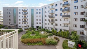 Un immeuble résidentiel à plusieurs étages, doté de balcons, d’une cour intérieure verdoyante et surplombant un ciel dégagé.