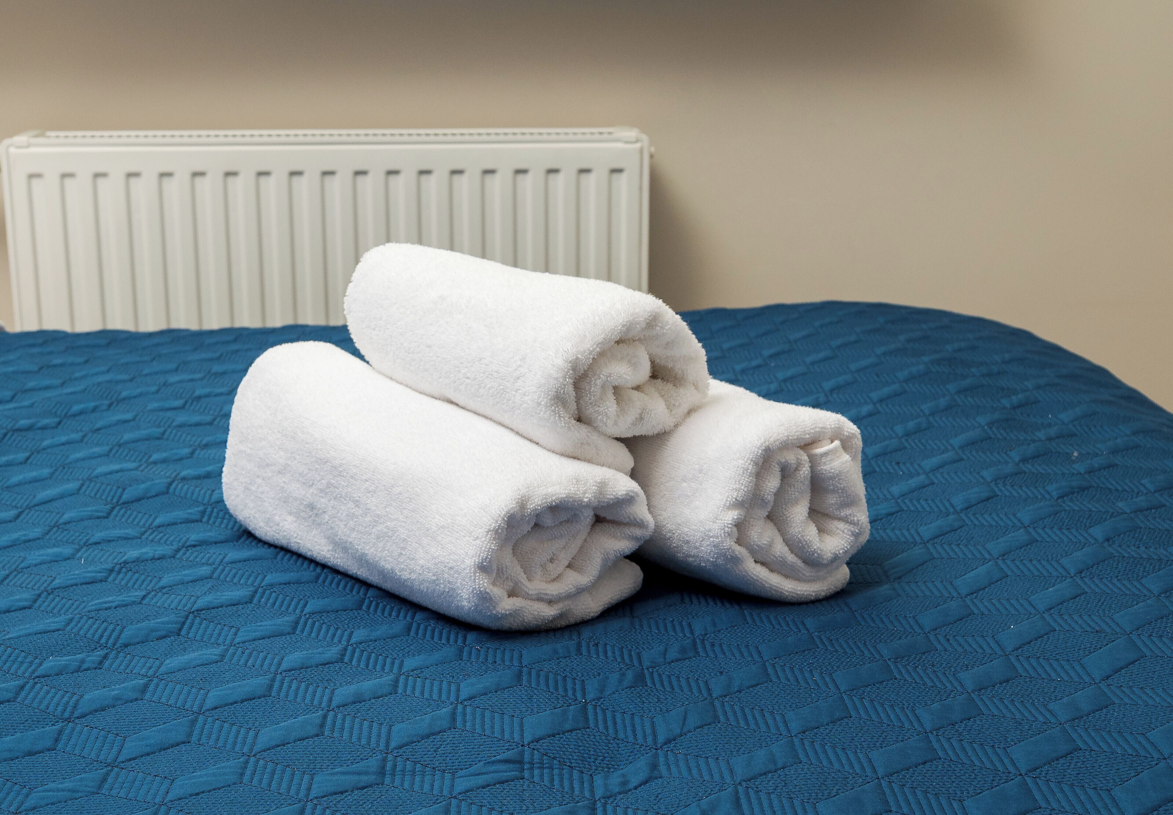 Un lit recouvert d’une couette bleue, avec deux serviettes blanches enroulées posées dessus.