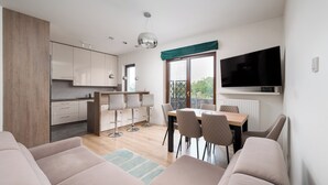 Un salon moderne comprenant un canapé, une table à manger avec des chaises, un coin cuisine avec des placards et un téléviseur fixé au mur.