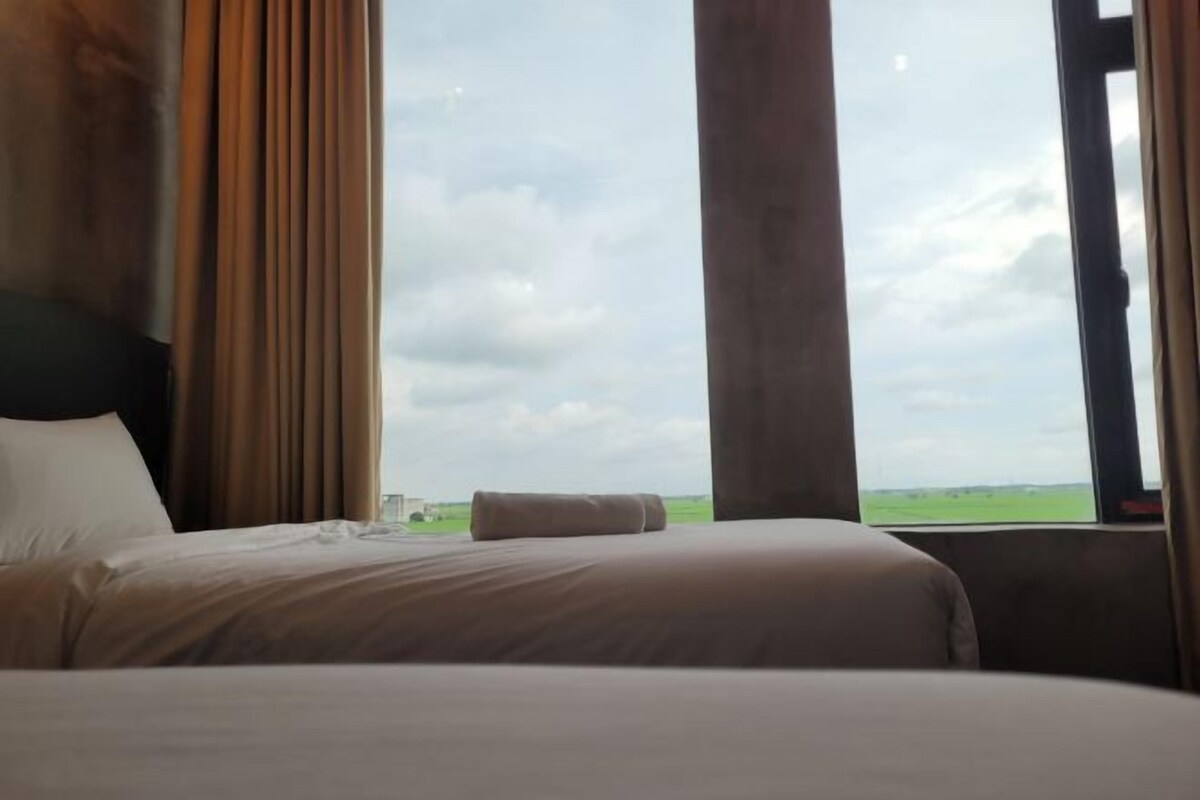 Ein Hotelzimmer mit Bett, Vorhängen und Blick auf Himmel und Landschaft.