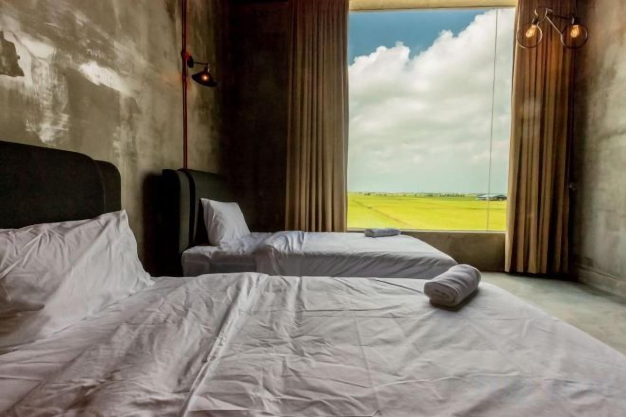 A hotel room with two beds, a large window with a view of a field, and a curtain.