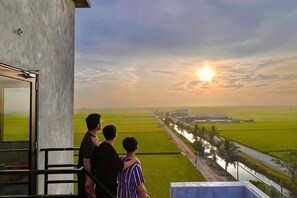 Uma varanda com vista para um pôr do sol sobre um campo verde.