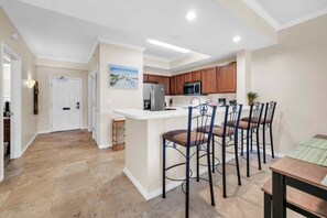Una cocina con una isla central, taburetes de bar, un refrigerador y un microondas.