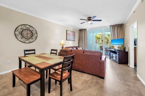 Un'area pranzo con tavolo e sedie in legno, un divano, una ventola a soffitto e una TV sullo sfondo.
