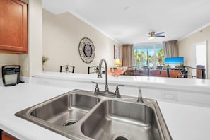 Una cocina con un lavamanos doble, ventilador de techo y vistas al área de estar, que incluye un televisor y asientos exteriores.