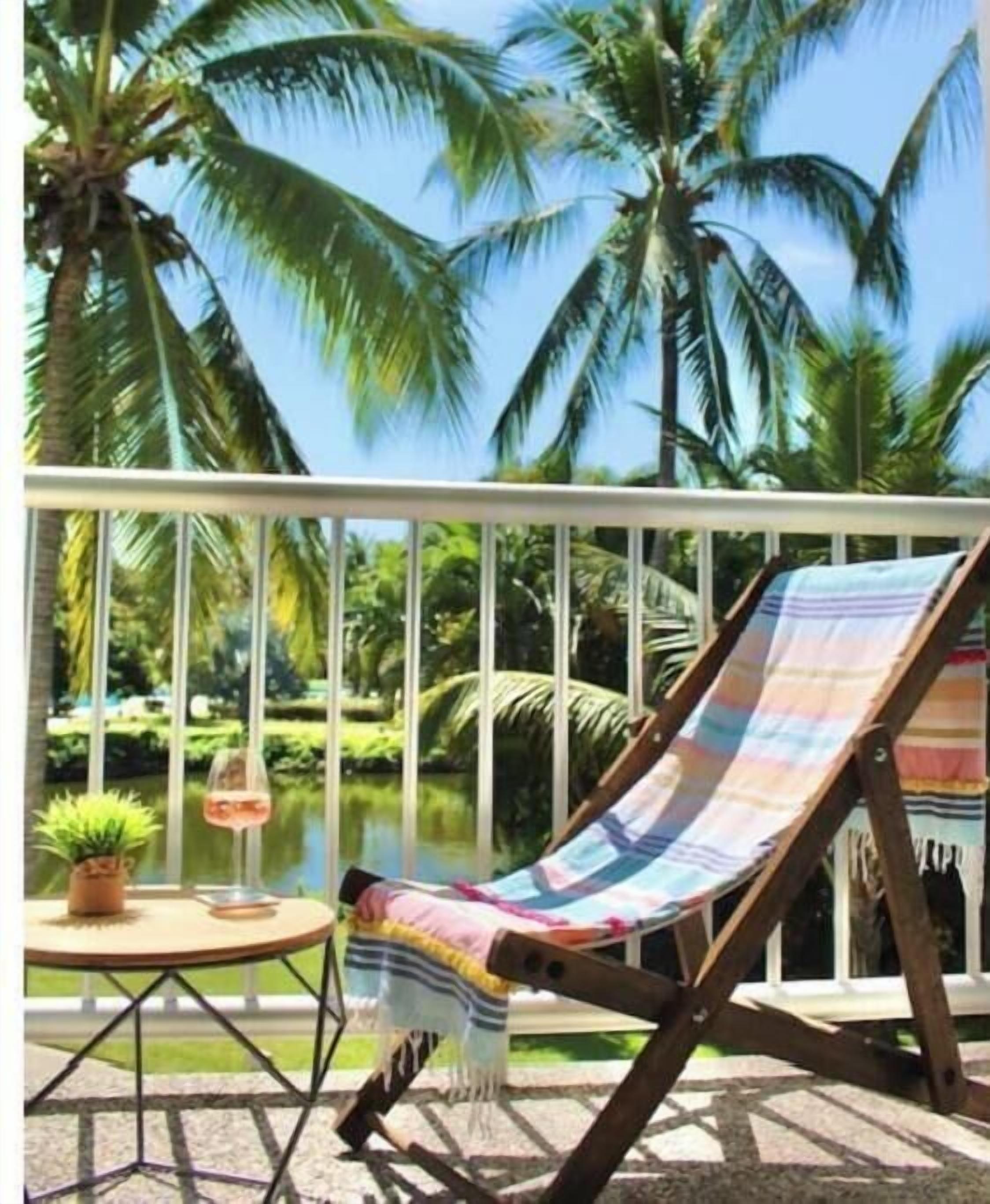A balcony with a hammock, a small table with a potted plant, and a glass of wine.