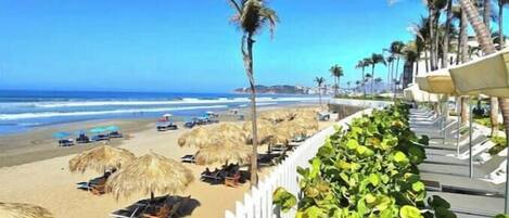 Una playa con palmeras, sombrillas y sillas de descanso.