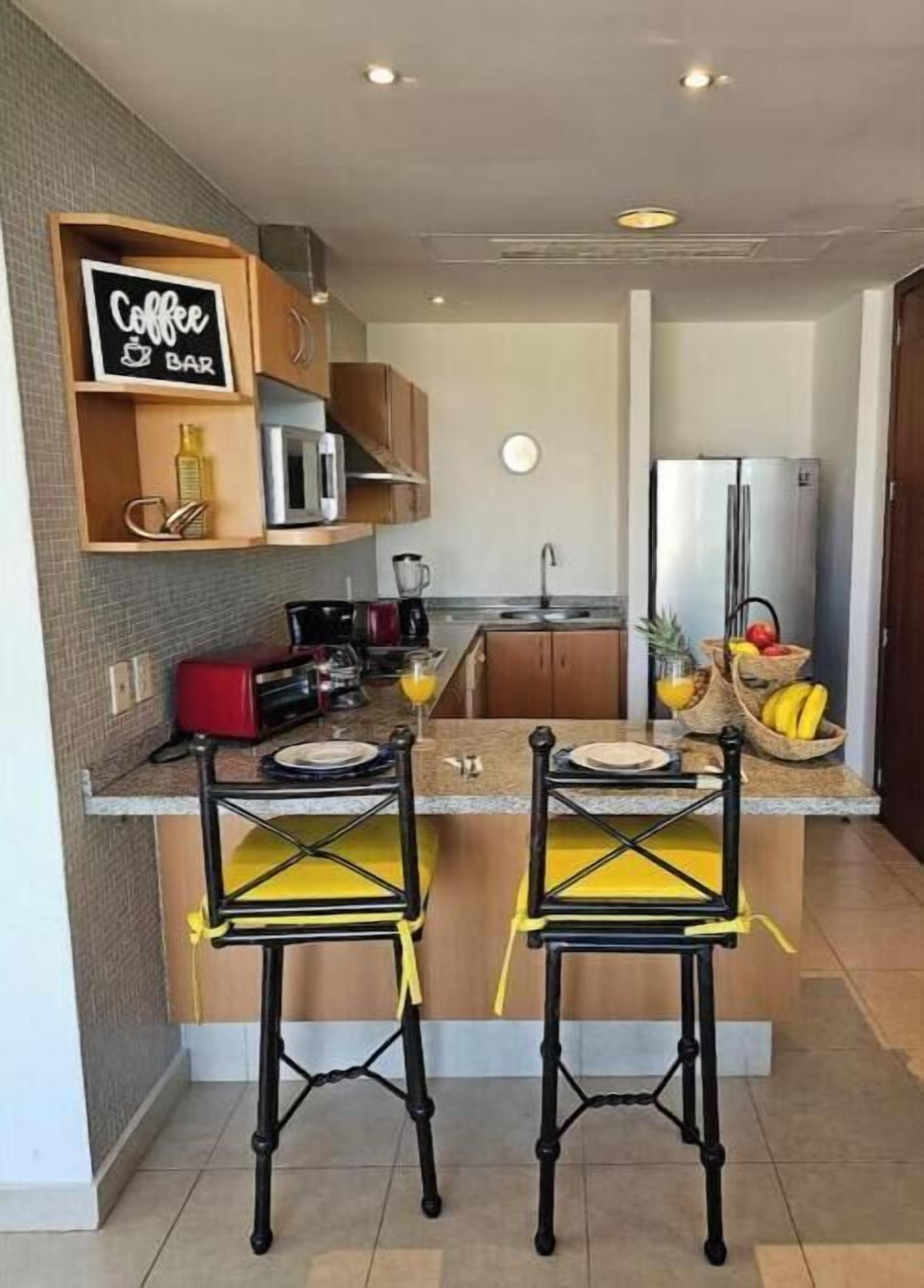 A compact kitchen with a coffee bar sign, a microwave, a refrigerator, and a fruit bowl.