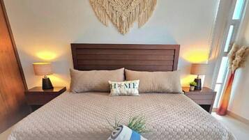 Une chambre avec un grand lit, deux tables de chevet et une décoration murale en macramé.