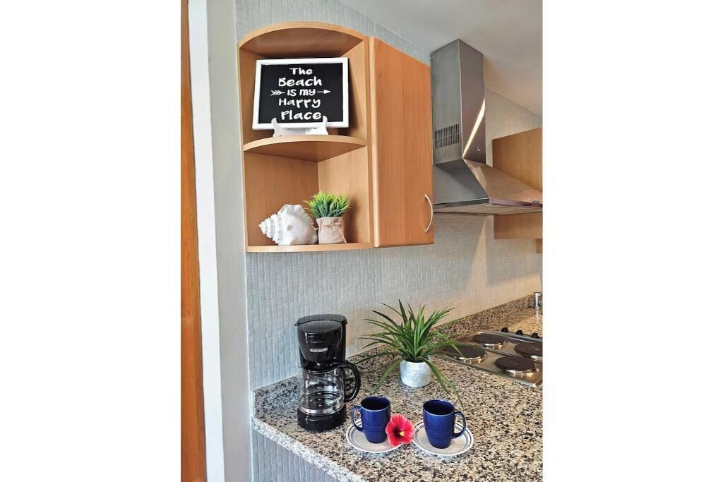 A kitchen with a coffee maker, two mugs, a potted plant, and a sign that reads "The Beach is my Harry Potter Place".
