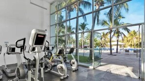 Une salle de sport équipée de machines de cardio et dotée de grandes fenêtres donnant sur des palmiers.