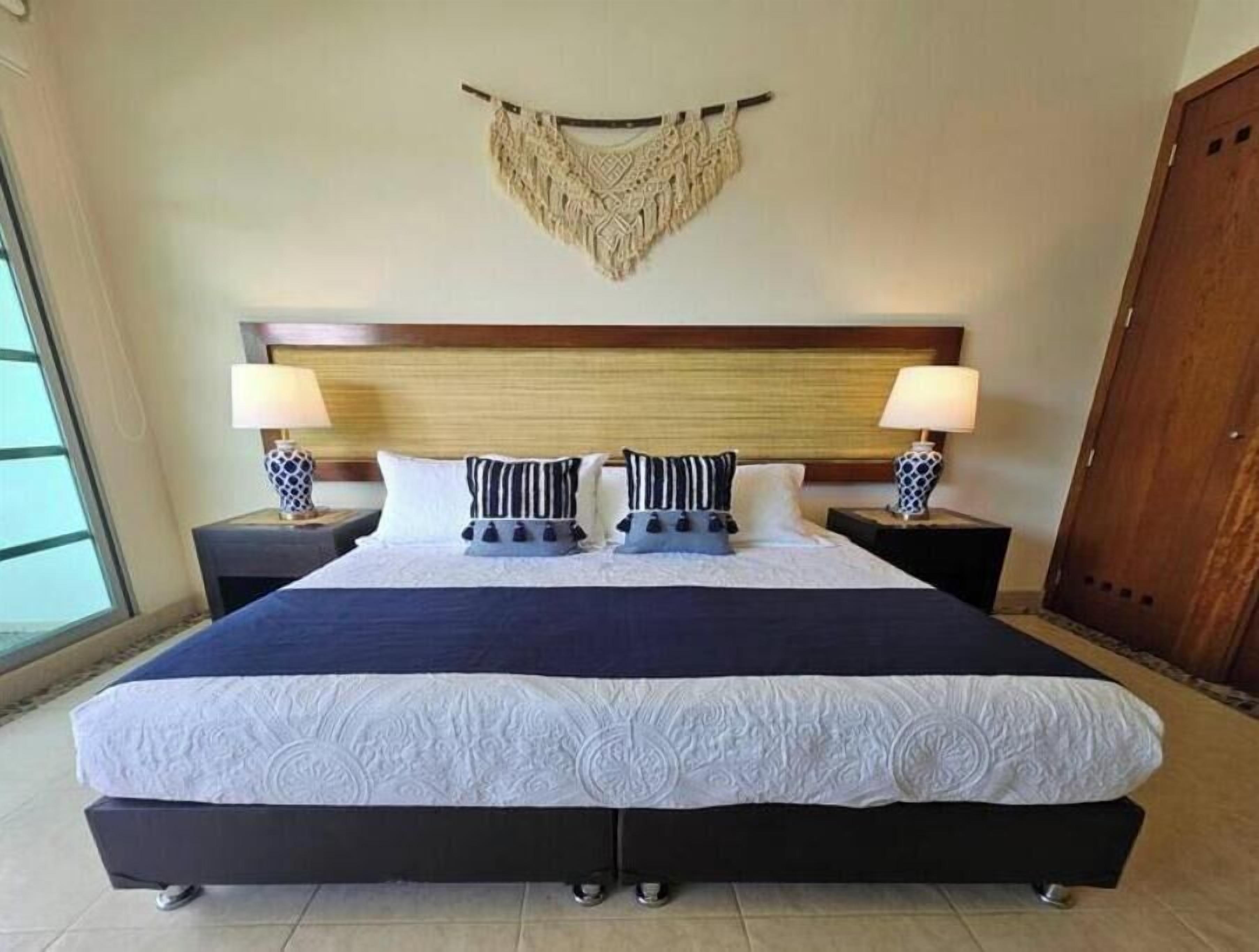 A double bed with a dark headboard, two bedside tables with lamps, and a decorative wall hanging.