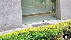 Ein moderner Gebäudeeingang mit Glastür, einem kleinen Fenster und einem Sicherheitstastaturfeld.